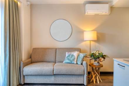 Salon d’un appart-hôtel avec canapé confortable, coussins décoratifs, lampe d’ambiance et miroir mural près de Colmar, en Alsace