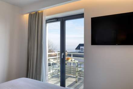 Chambre d’un appart-hôtel avec baie vitrée donnant sur un balcon et vue extérieure près de Colmar, en Alsace