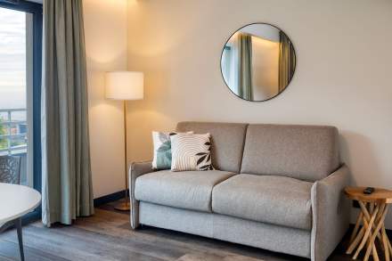 Salon d’un appart-hôtel 4 étoiles avec canapé confortable, lampe d’ambiance et miroir mural près de Colmar, en Alsace, aux Appartements Husseren Collections