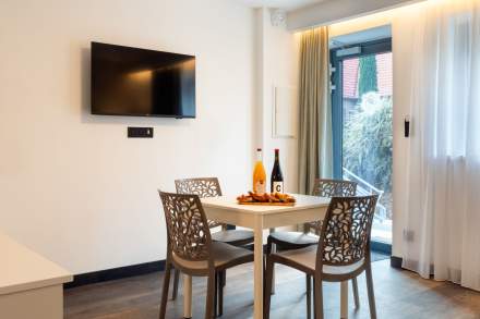 Coin repas d’un appart-hôtel avec table, chaises design, télévision murale et accès extérieur près de Colmar, en Alsace