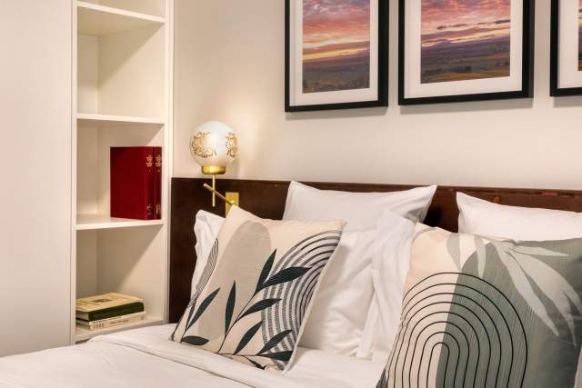 Detailansicht eines Doppelbetts in einem Aparthotel mit dekorativen Kissen, stimmungsvoller Beleuchtung und Bilderrahmen in der Nähe von Colmar im Elsass, in den Appartements Husseren Collections.