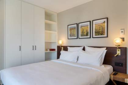 Chambre d’un appart-hôtel avec lit double, linge blanc, rangements intégrés et cadres décoratifs près de Colmar, en Alsace