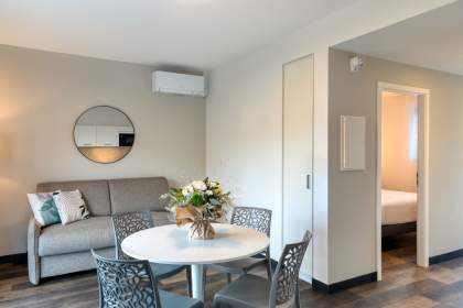 Séjour d’un appart-hôtel avec coin repas, canapé confortable, miroir mural et climatisation près de Colmar, en Alsace