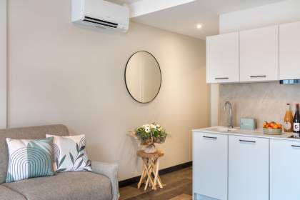 Living area of a serviced apartment with sofa, fully equipped kitchenette, wall mirror, and air conditioning near Colmar, Alsace – Husseren Collections Apartments