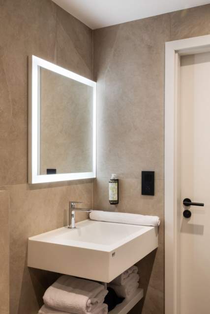 Badezimmer eines Aparthotels mit Waschbecken, beleuchtetem Spiegel und moderner Innentür in der Nähe von Colmar im Elsass