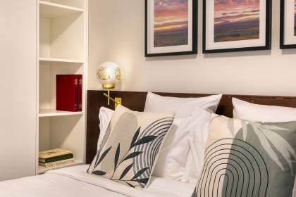 Détail du lit double d’un appart-hôtel avec coussins décoratifs, éclairage d’ambiance et cadres muraux près de Colmar, en Alsace