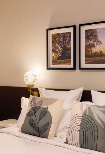 Tête de lit d’un appart-hôtel avec coussins décoratifs, lampe d’ambiance et cadres muraux près de Colmar, en Alsace