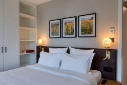 Chambre élégante avec lit double habillé de linge blanc, têtes de lit foncées, lampes d’ambiance et cadres décoratifs aux Appartements Husseren Collections 4 étoiles