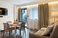 Séjour lumineux avec table à manger, fauteuil design, canapé confortable et baie vitrée habillée de rideaux aux Appartements Husseren Collections 4 étoiles