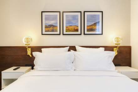 Lit double d’un appart-hôtel avec linge blanc, têtes de lit foncées et cadres décoratifs près de Colmar, en Alsace, aux Appartements Husseren Collections 4 étoiles