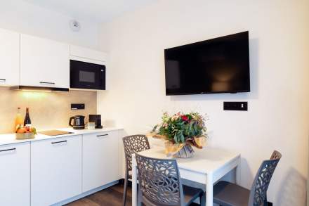 Coin repas avec table et chaises design, cuisine équipée intégrée et télévision murale aux Appartements Husseren Collections 4 étoiles