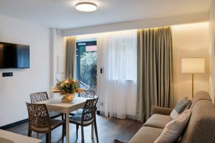 Séjour lumineux d’un appart-hôtel avec coin repas, canapé confortable et grandes baies vitrées près de Colmar, en Alsace