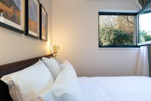 Zimmer in einem Aparthotel mit Doppelbett, weißer Bettwäsche, Stimmungslampe und Fenster mit Blick ins Grüne in der Nähe von Colmar im Elsass
