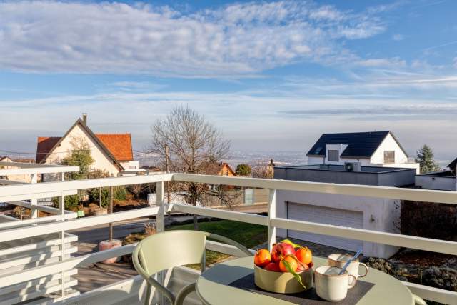 Terrasse eines Aparthotels mit Tisch, Stühlen, Obstkorb und freiem Blick über die Dächer und den Himmel in der Nähe von Colmar im Elsass