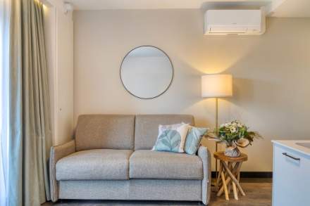 Salon cosy avec canapé clair, coussins décoratifs, lampe d’ambiance et miroir mural aux Appartements Husseren Collections 4 étoiles