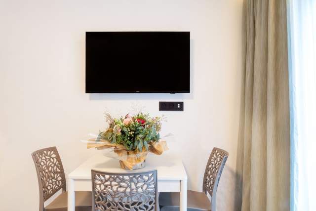 Essbereich eines Aparthotels mit Tisch, Designerstühlen, Wandfernseher und Blumendekoration in der Nähe von Colmar im Elsass