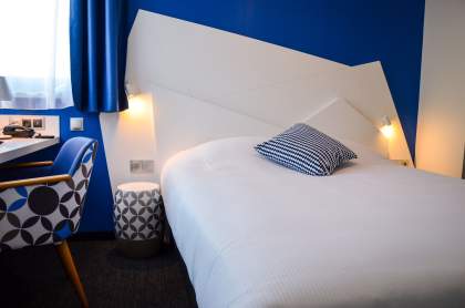 Hotelzimmer mit Doppelbett, Schreibtisch, Designersessel, stimmungsvoller Beleuchtung und Tageslicht im Elsass