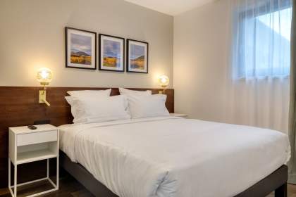 Chambre d’un appart-hôtel avec lit double, linge blanc, tables de chevet éclairées et cadres décoratifs près de Colmar, en Alsace