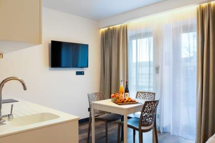 Coin repas lumineux d’un appart-hôtel avec table, chaises design, télévision murale et baie vitrée près de Colmar, en Alsace