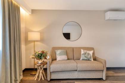 Salon d’un appart-hôtel avec canapé confortable, coussins décoratifs, lampe d’ambiance et miroir mural près de Colmar, en Alsace