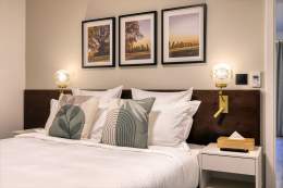 Double bed in a serviced apartment with decorative cushions, dark headboard, and ambient lighting near Colmar, Alsace – Husseren Collections Apartments