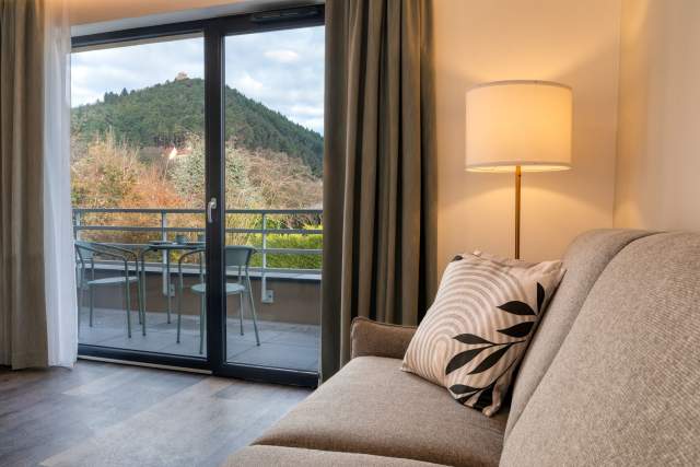 Wohnzimmer eines Aparthotels mit Sofa, Stimmungslampe und Erkerfenster mit Blick auf die Terrasse und die elsässischen Hügel in der Nähe von Colmar im Elsass