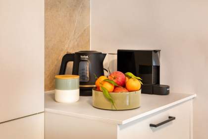 Plan de travail d’une cuisine d’appart-hôtel avec cafetière, bouilloire, corbeille de fruits et produits d’accueil près de Colmar, en Alsace